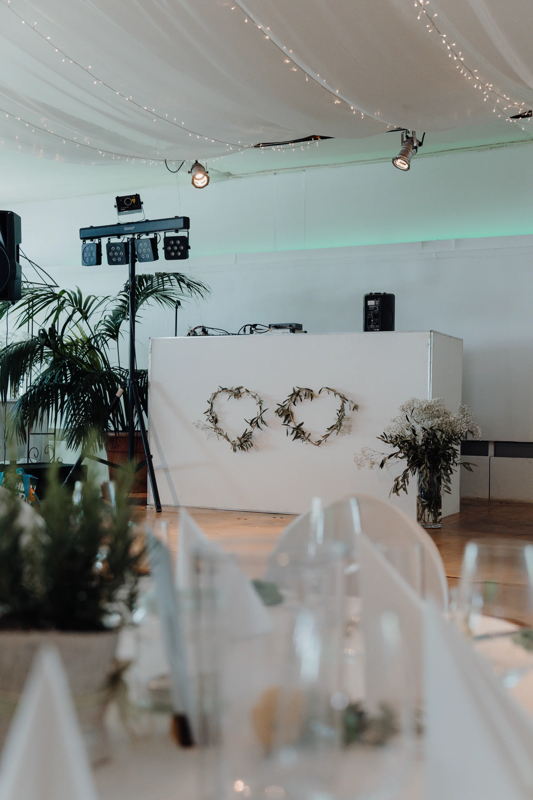 Weißes DJ-Pult bei einer Hochzeit in Köln, dekoriert mit zwei Herzen aus Zweigen und umrahmt von Blumen