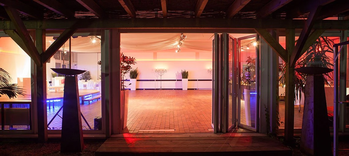 Abendliche Eventlocation in Köln, Blick von außen in festlich beleuchteten Saal mit offener Glastür und Lichtakzenten