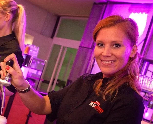 Mitarbeiterin von Tafelfreuden zapft Bier an der Theke in Köln und lächelt freundlich in die Kamera